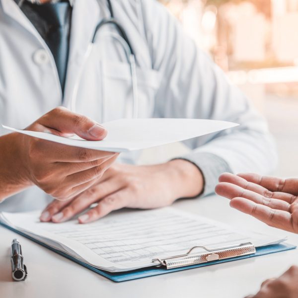 Doctor or physician writing diagnosis and giving a medical prescription to male Patient