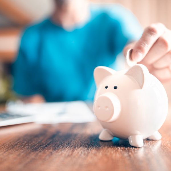 Man putting a coin into a pink piggy bank concept for savings and finance