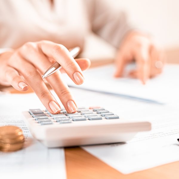 Woman using a calculator doing a balance of monthly expenses. Close up of businesswoman working with financial data and using calculator with coins on desk at office. Deatil of hands calculating home finances and annual taxes.