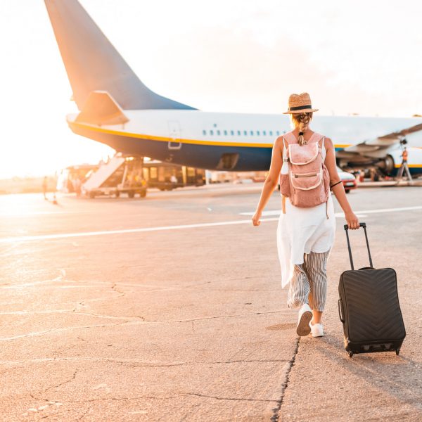 A female tourist walks towards the plane on the runway, dragging personal luggage behind her and carrying a backpack on her back