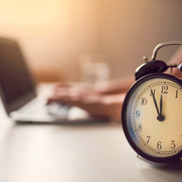 Unrecognizable woman working at the laptop computer; retro alarm clock and a glass of water next to her